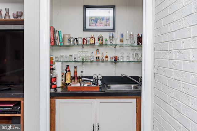 bar with white cabinetry, sink, and brick wall