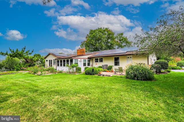 rear view of house with central AC unit, solar panels, and a yard