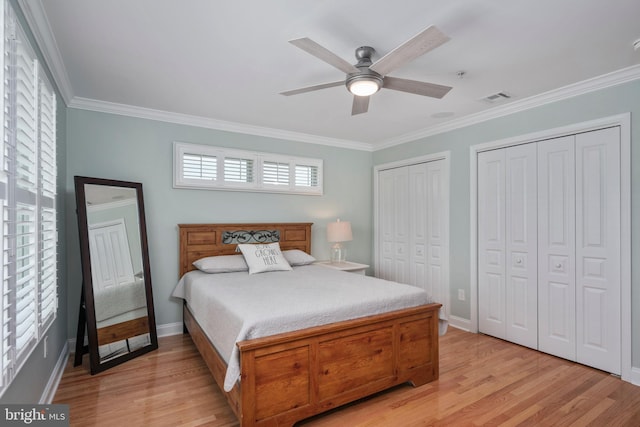 bedroom with ornamental molding, multiple closets, light hardwood / wood-style floors, and ceiling fan