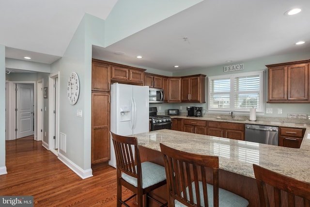 kitchen with light stone counters, dark wood-type flooring, sink, a breakfast bar area, and appliances with stainless steel finishes