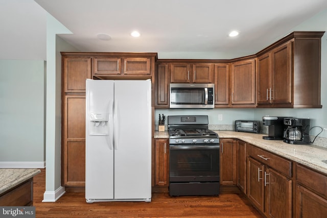 kitchen featuring gas range, white fridge with ice dispenser, dark wood-type flooring, and light stone counters