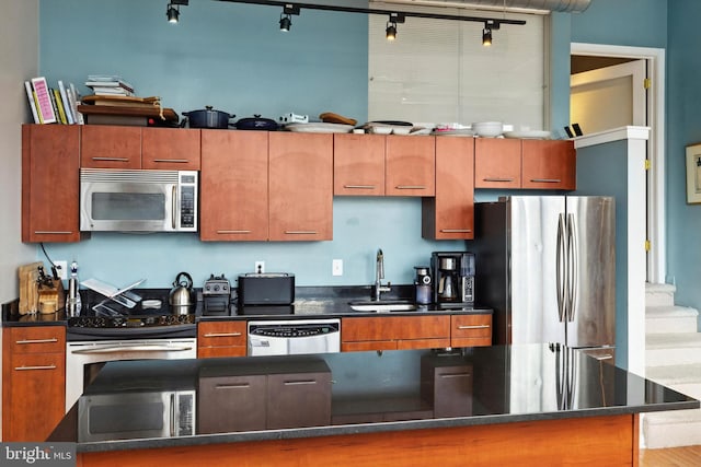 kitchen with brown cabinetry, track lighting, appliances with stainless steel finishes, and a sink
