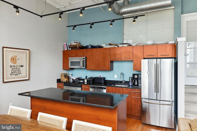 kitchen with a sink, a kitchen island, dark countertops, appliances with stainless steel finishes, and a towering ceiling