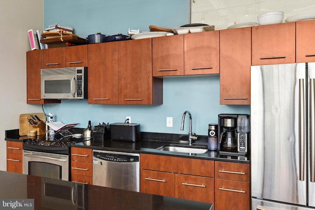 kitchen with a sink, stainless steel appliances, dark countertops, and brown cabinetry