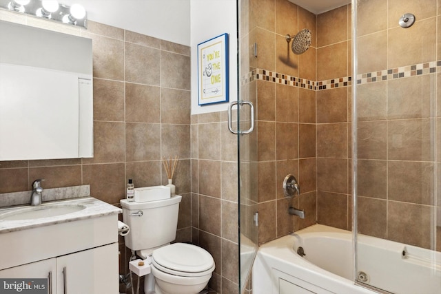 bathroom featuring combined bath / shower with glass door, toilet, vanity, and tile walls