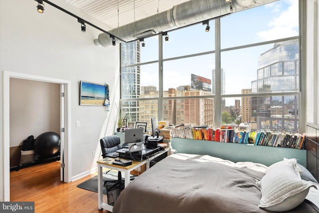 bedroom featuring baseboards, a city view, wood finished floors, and track lighting