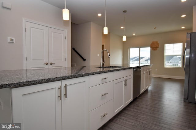 kitchen with appliances with stainless steel finishes, sink, white cabinetry, dark stone counters, and pendant lighting