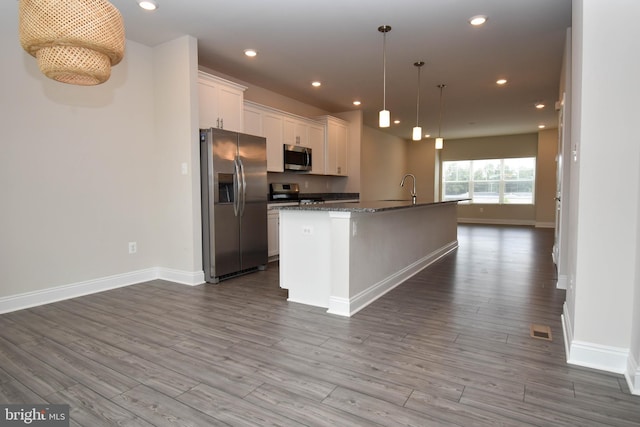 kitchen featuring light hardwood / wood-style flooring, stainless steel appliances, a center island with sink, pendant lighting, and white cabinets