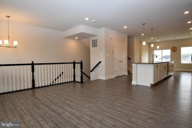 kitchen with dark wood-type flooring, a kitchen island with sink, decorative light fixtures, and white cabinetry