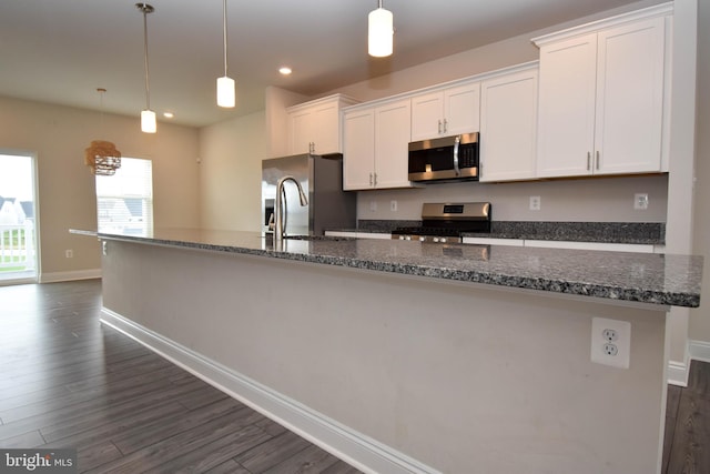 kitchen featuring white cabinets, hanging light fixtures, stainless steel appliances, and an island with sink