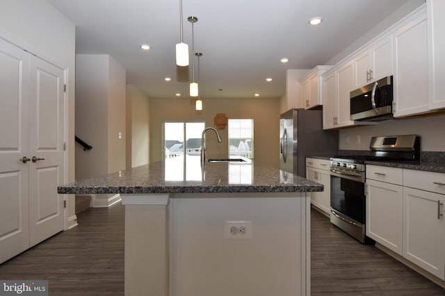 kitchen with a center island with sink, stainless steel appliances, dark wood-type flooring, sink, and decorative light fixtures