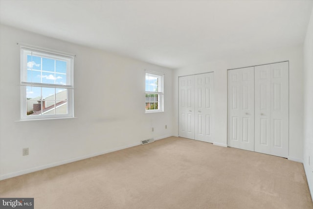 unfurnished bedroom featuring multiple windows, light carpet, and multiple closets