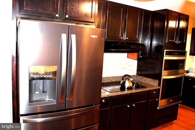 kitchen with wood-type flooring, stainless steel appliances, light stone countertops, and dark brown cabinets