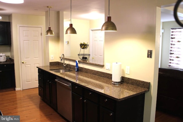 kitchen featuring hanging light fixtures, dark stone countertops, hardwood / wood-style floors, sink, and stainless steel dishwasher