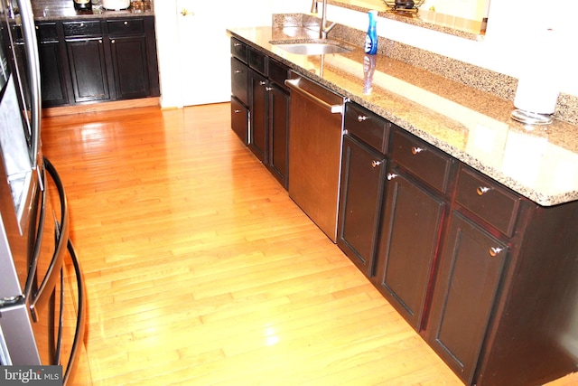 kitchen with light wood-type flooring, light stone countertops, stainless steel appliances, and sink