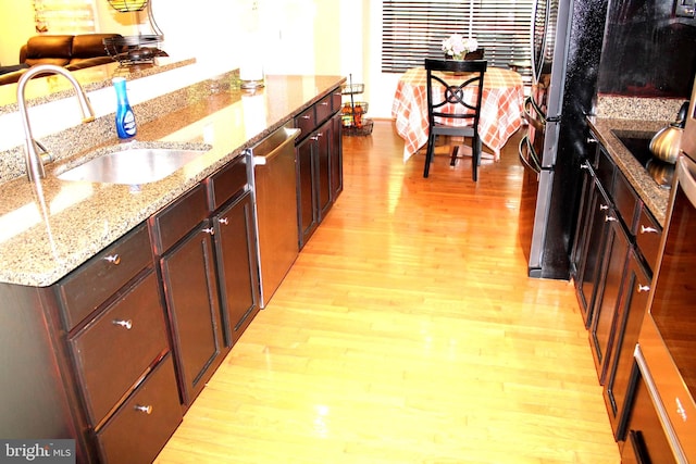 kitchen with light hardwood / wood-style flooring, light stone counters, sink, and appliances with stainless steel finishes