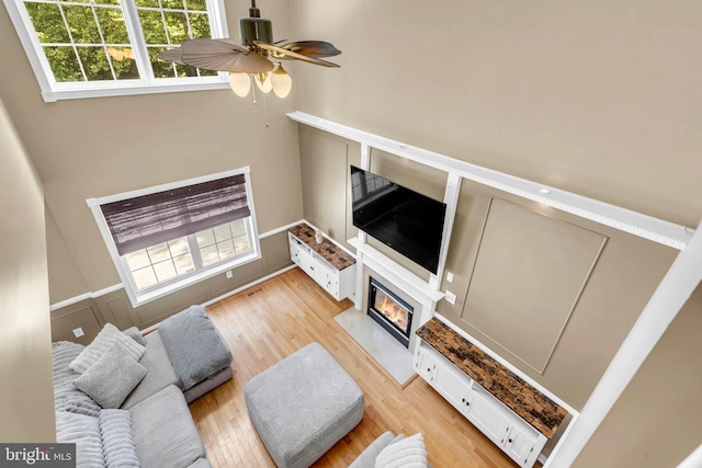 living room with light wood-type flooring, ceiling fan, a wealth of natural light, and a towering ceiling