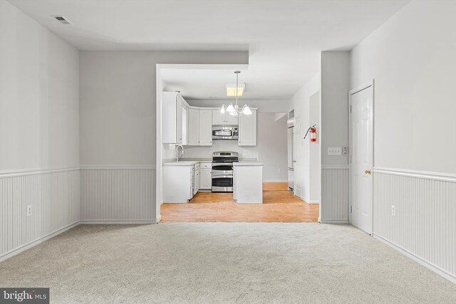 kitchen featuring white cabinets, light colored carpet, an inviting chandelier, appliances with stainless steel finishes, and decorative light fixtures