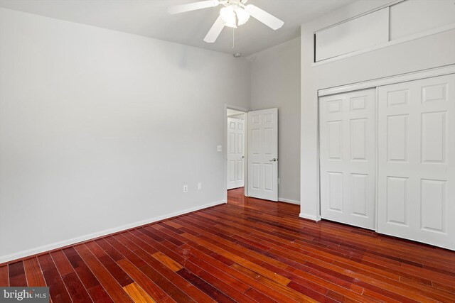 unfurnished bedroom featuring ceiling fan, a closet, a towering ceiling, and dark hardwood / wood-style flooring