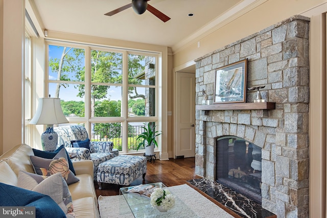 living room featuring ceiling fan, a stone fireplace, ornamental molding, and dark hardwood / wood-style flooring