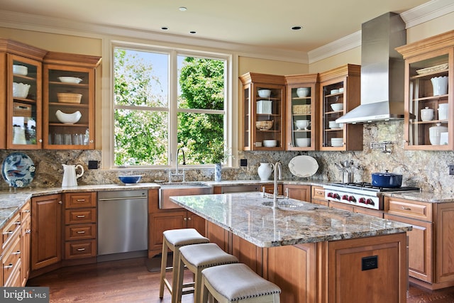 kitchen with light stone countertops, a center island with sink, and wall chimney range hood