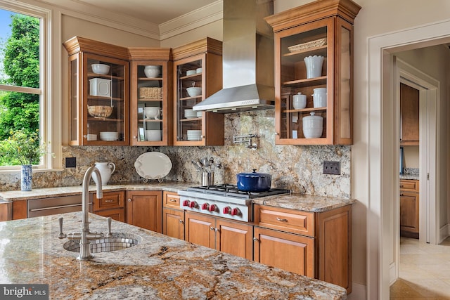 kitchen with light stone counters, ornamental molding, sink, wall chimney exhaust hood, and stainless steel gas stovetop