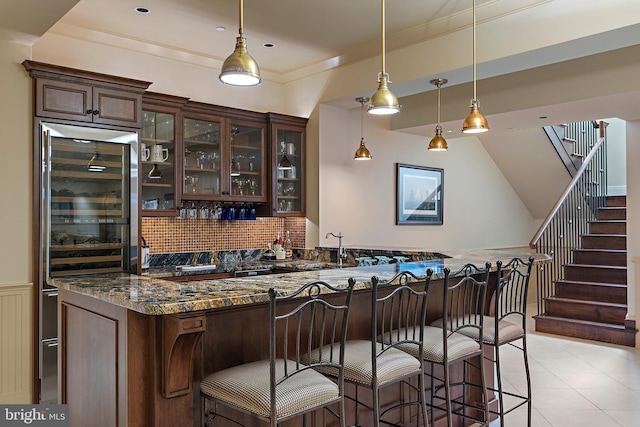 bar with dark brown cabinetry, pendant lighting, wine cooler, dark stone countertops, and decorative backsplash