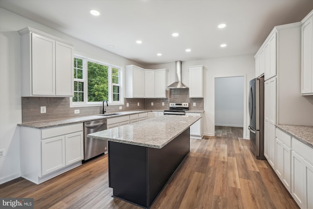 kitchen with sink, a kitchen island, wood-type flooring, wall chimney range hood, and stainless steel appliances