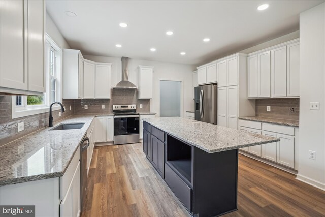 kitchen with sink, white cabinets, a kitchen island, wall chimney range hood, and stainless steel appliances