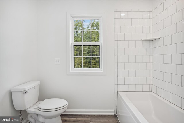 bathroom with hardwood / wood-style floors, toilet, and tiled shower / bath