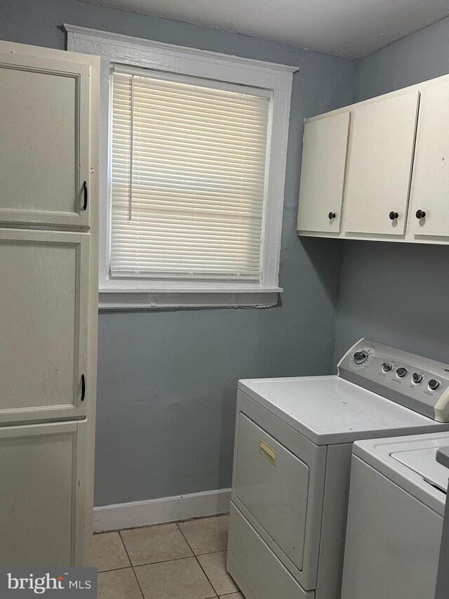 clothes washing area featuring separate washer and dryer, cabinets, and light tile patterned flooring