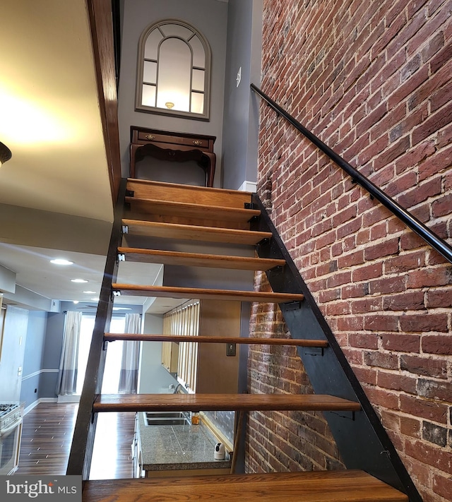 stairs featuring a high ceiling, brick wall, and hardwood / wood-style floors