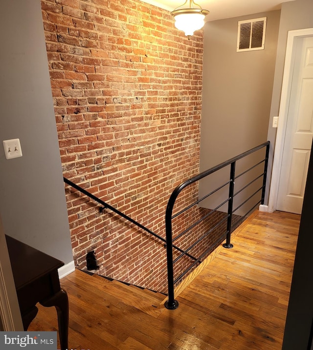 staircase with brick wall and hardwood / wood-style floors