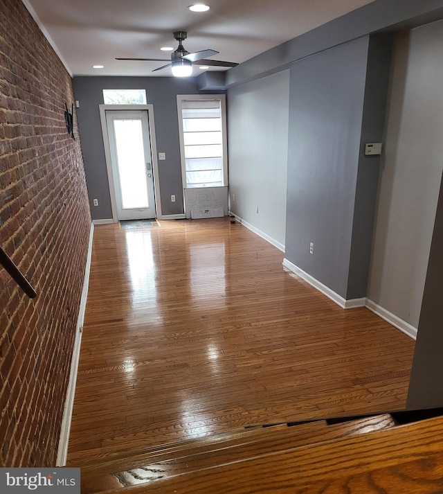 interior space featuring ceiling fan, brick wall, and hardwood / wood-style floors