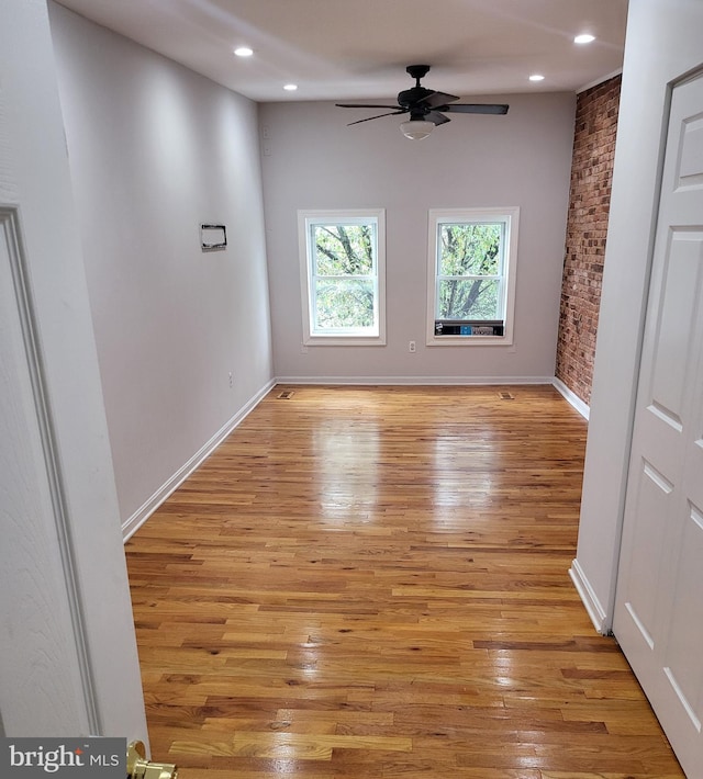 unfurnished room featuring light wood-type flooring, ceiling fan, and brick wall