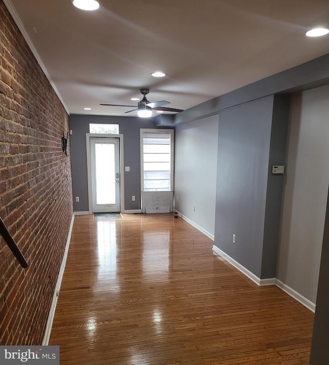 empty room featuring ceiling fan, ornamental molding, brick wall, and wood-type flooring