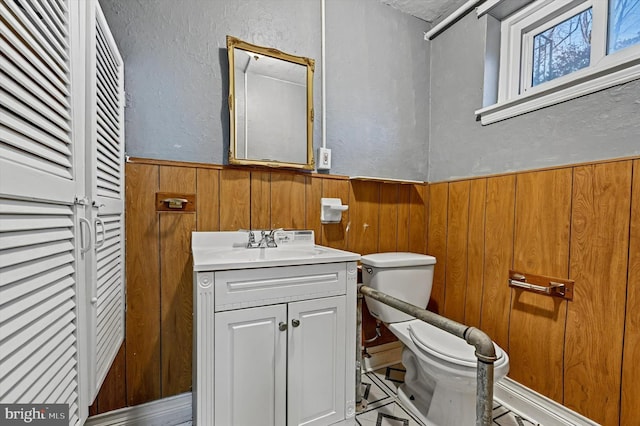 bathroom with wood walls, vanity, and toilet