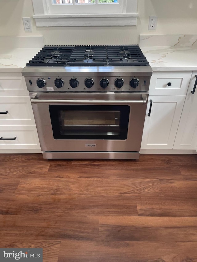 interior space featuring dark hardwood / wood-style floors, high end stove, light stone countertops, and white cabinets