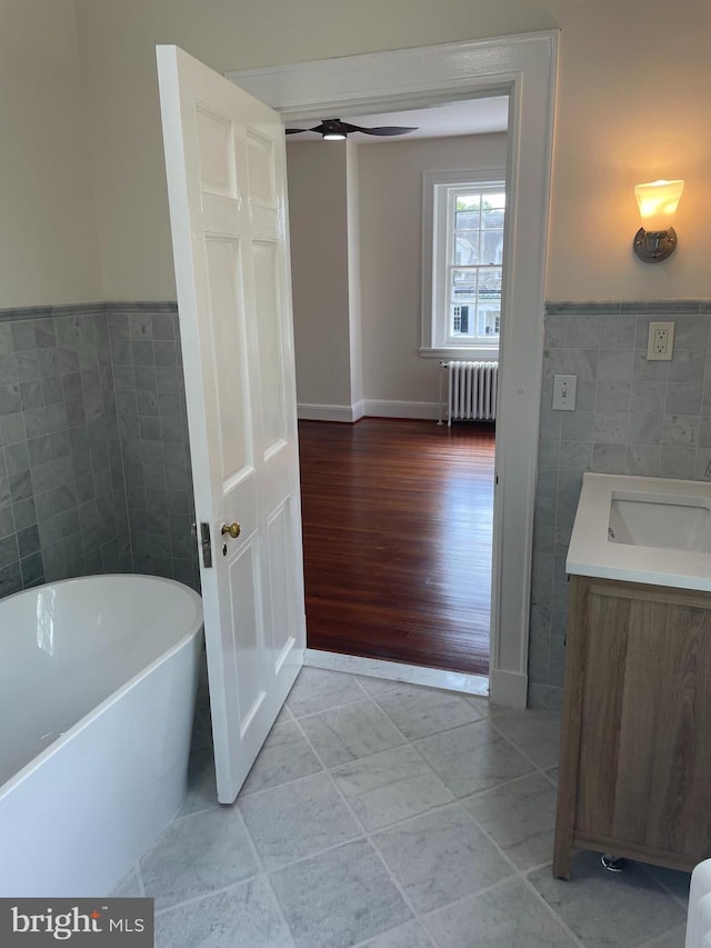 bathroom with ceiling fan, vanity, radiator heating unit, a tub, and wood-type flooring