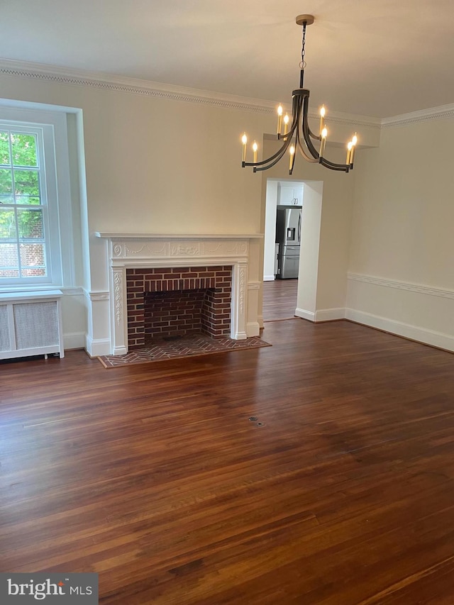 unfurnished living room featuring a brick fireplace, dark wood-type flooring, a chandelier, and radiator heating unit