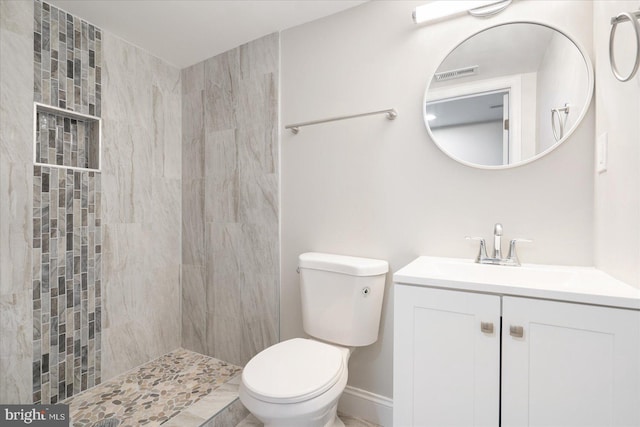 bathroom featuring a tile shower, vanity, and toilet