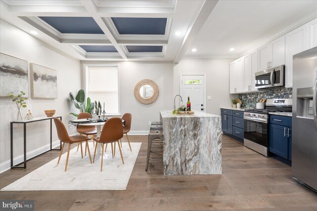 kitchen with blue cabinets, white cabinetry, stainless steel appliances, wood-type flooring, and a kitchen island with sink