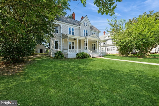 view of front of house with an outbuilding, a porch, ceiling fan, a chimney, and a front lawn