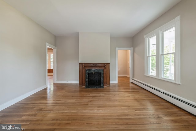 unfurnished living room with a baseboard heating unit, a premium fireplace, and light hardwood / wood-style floors