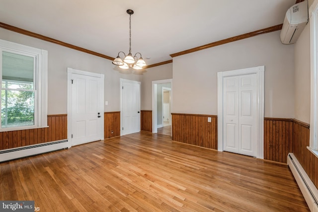 spare room featuring a baseboard heating unit, ornamental molding, light wood-type flooring, and a wall mounted air conditioner