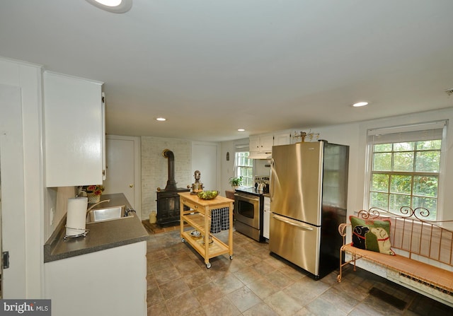 kitchen with stainless steel appliances, a wood stove, sink, and white cabinets