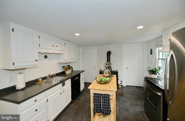 kitchen with black appliances, sink, a wood stove, dark tile patterned floors, and white cabinets