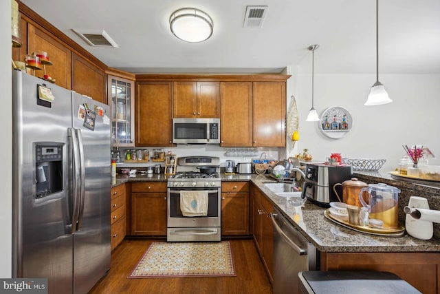 kitchen featuring hanging light fixtures, sink, stainless steel appliances, dark stone countertops, and dark hardwood / wood-style flooring