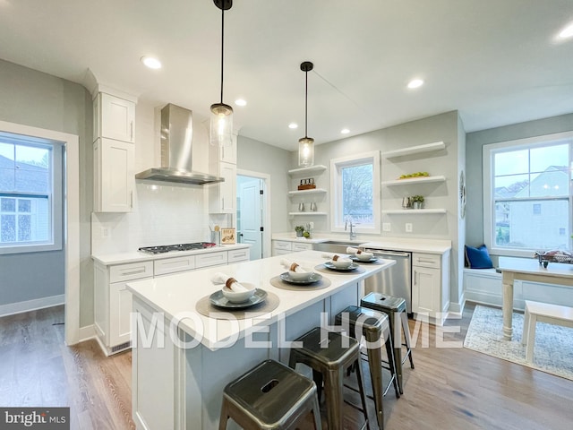 kitchen featuring appliances with stainless steel finishes, a center island, white cabinetry, and wall chimney range hood