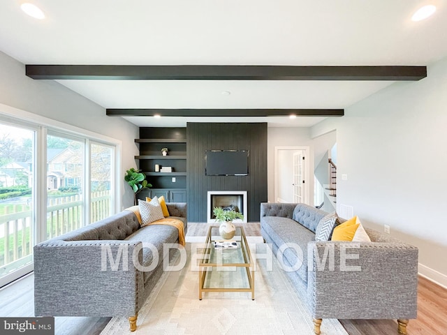 living room featuring beamed ceiling, a large fireplace, light hardwood / wood-style floors, and built in features